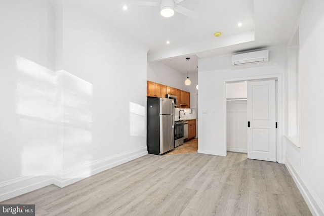 kitchen with pendant lighting, sink, light hardwood / wood-style flooring, appliances with stainless steel finishes, and a wall unit AC