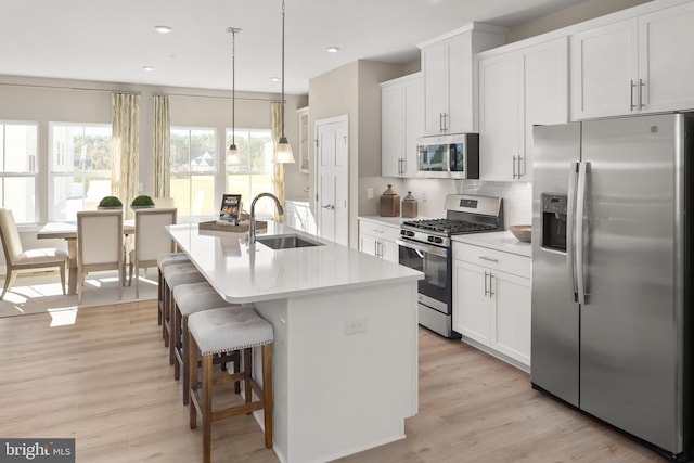 kitchen featuring a kitchen island with sink, white cabinets, sink, decorative light fixtures, and stainless steel appliances