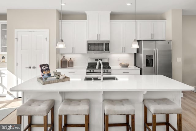 kitchen with appliances with stainless steel finishes, light hardwood / wood-style floors, white cabinetry, and a kitchen island with sink