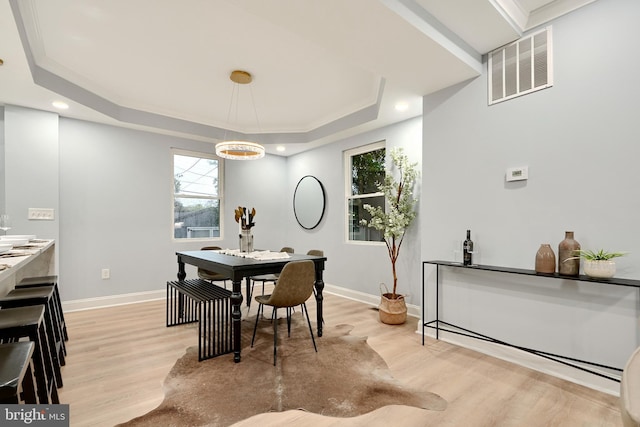 dining space with light wood-type flooring, a raised ceiling, and crown molding