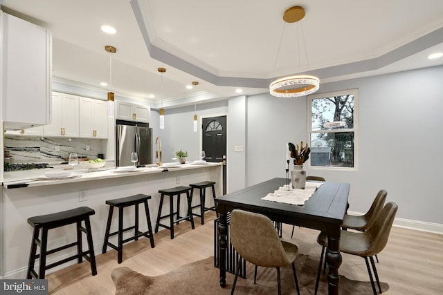 dining area featuring a tray ceiling, sink, ornamental molding, and light wood-type flooring