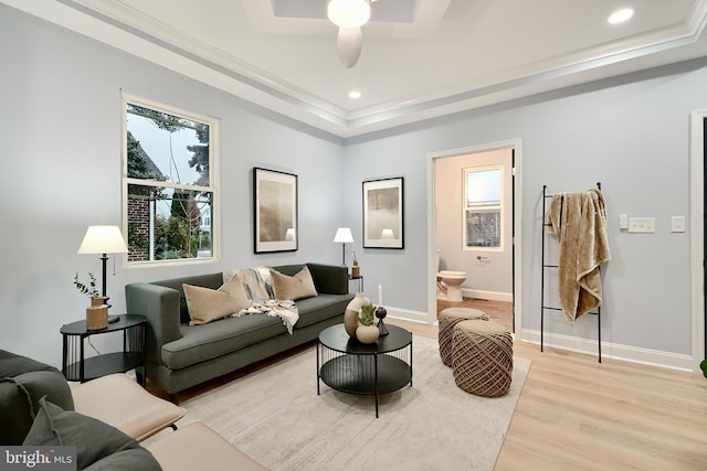 living room featuring light wood-type flooring, a tray ceiling, ceiling fan, and crown molding