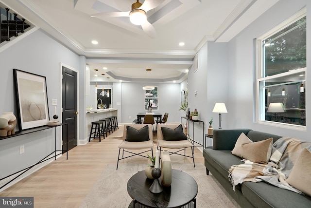 living room with a tray ceiling, ceiling fan, light hardwood / wood-style flooring, and ornamental molding