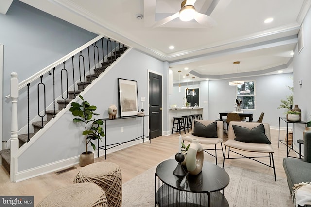 living room with a tray ceiling, ceiling fan, light hardwood / wood-style flooring, and ornamental molding