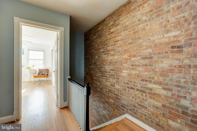 hallway with light hardwood / wood-style floors and brick wall