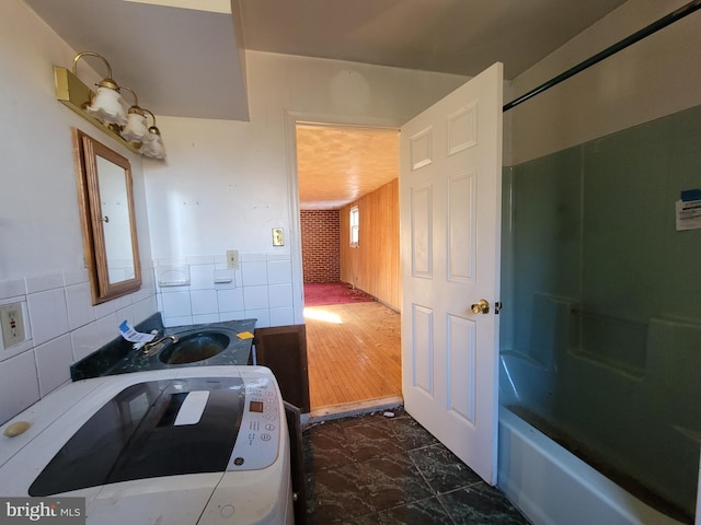 bathroom featuring shower / washtub combination, sink, hardwood / wood-style flooring, tile walls, and washer / clothes dryer