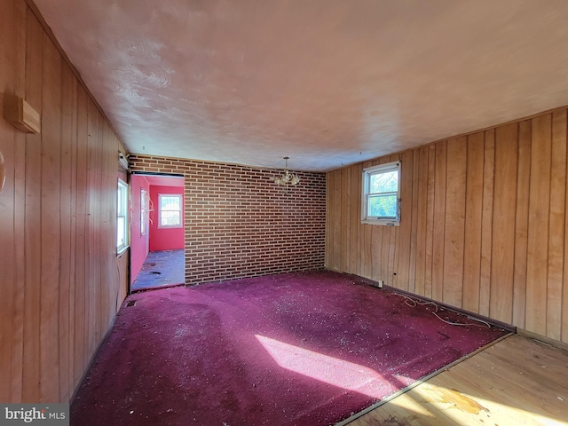 unfurnished room featuring light wood-type flooring, an inviting chandelier, wooden walls, and brick wall