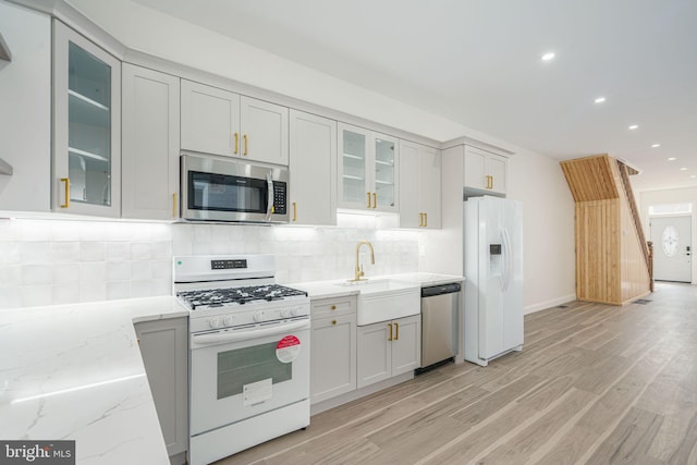 kitchen featuring sink, decorative backsplash, appliances with stainless steel finishes, light hardwood / wood-style floors, and light stone counters