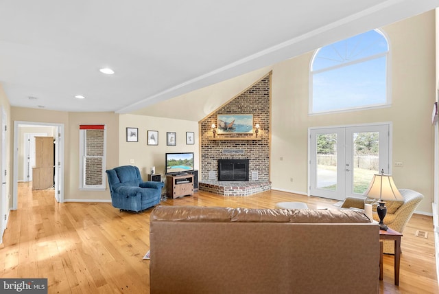 living room featuring french doors, high vaulted ceiling, a brick fireplace, and light wood-type flooring