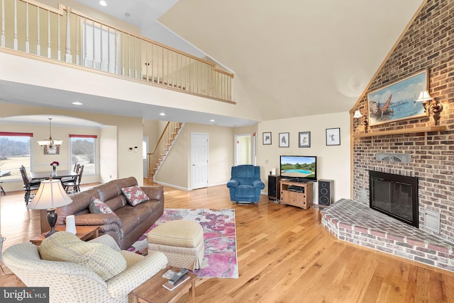 living room featuring high vaulted ceiling, a brick fireplace, an inviting chandelier, and light hardwood / wood-style floors