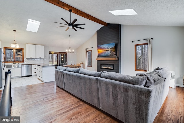 living area with a notable chandelier, a fireplace, light wood-style flooring, lofted ceiling with beams, and a textured ceiling