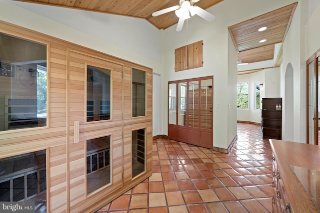 tiled foyer entrance with ceiling fan, a large fireplace, wooden ceiling, and high vaulted ceiling