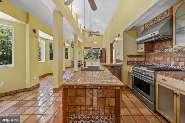 kitchen with decorative backsplash, wall chimney exhaust hood, high end stove, vaulted ceiling, and sink