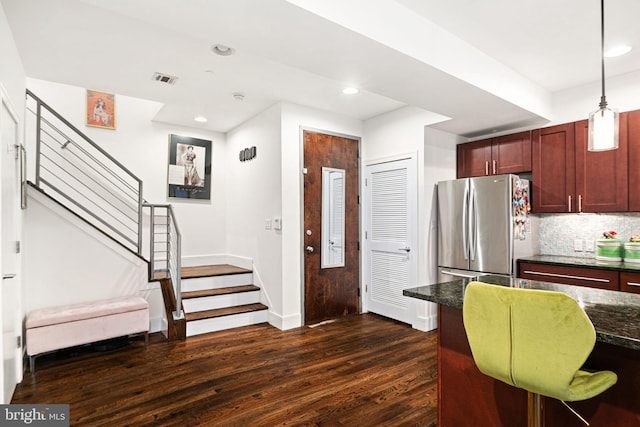 kitchen featuring stainless steel fridge, decorative backsplash, hanging light fixtures, and dark wood-type flooring