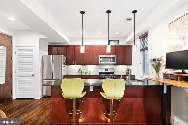 kitchen with appliances with stainless steel finishes, backsplash, dark wood-type flooring, sink, and hanging light fixtures