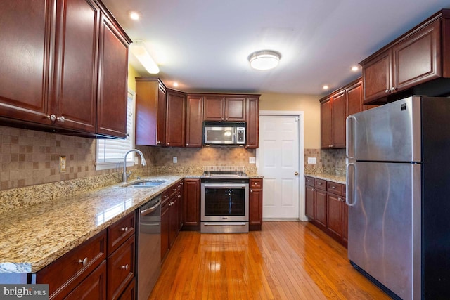 kitchen with tasteful backsplash, light stone counters, stainless steel appliances, sink, and light hardwood / wood-style floors