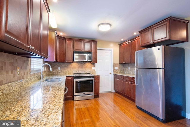 kitchen with sink, light stone counters, light hardwood / wood-style flooring, backsplash, and appliances with stainless steel finishes