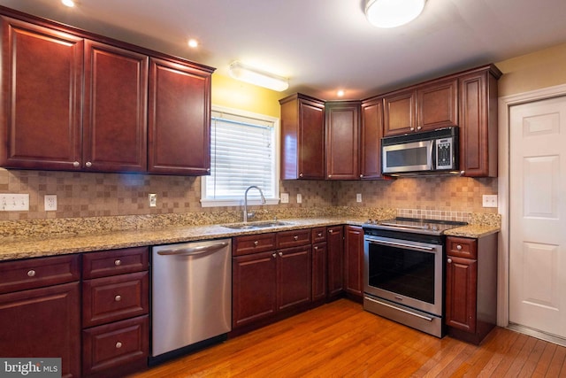 kitchen featuring sink, light hardwood / wood-style flooring, decorative backsplash, light stone countertops, and stainless steel appliances