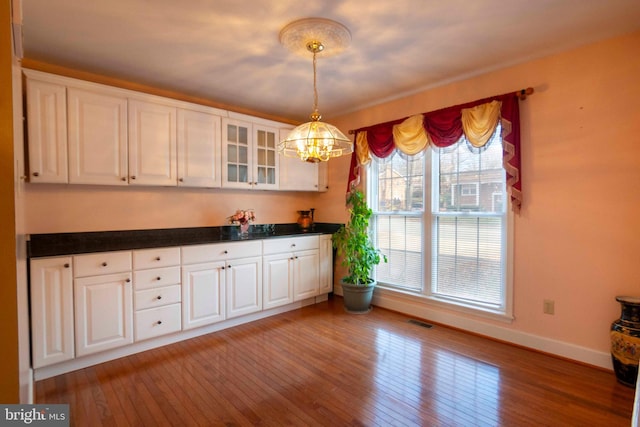 kitchen featuring white cabinets, a notable chandelier, light wood-type flooring, and hanging light fixtures