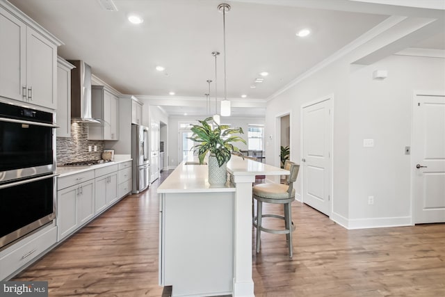 kitchen featuring decorative backsplash, wall chimney exhaust hood, stainless steel appliances, pendant lighting, and an island with sink