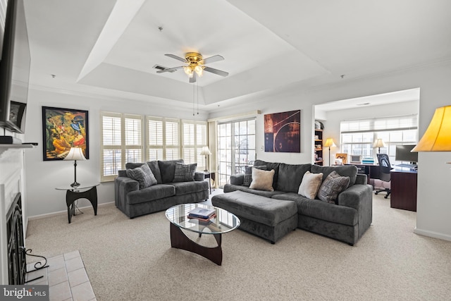 living room featuring plenty of natural light, light colored carpet, a raised ceiling, and ceiling fan