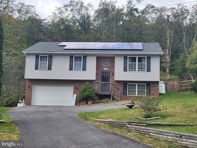 raised ranch featuring solar panels, a garage, and a front lawn