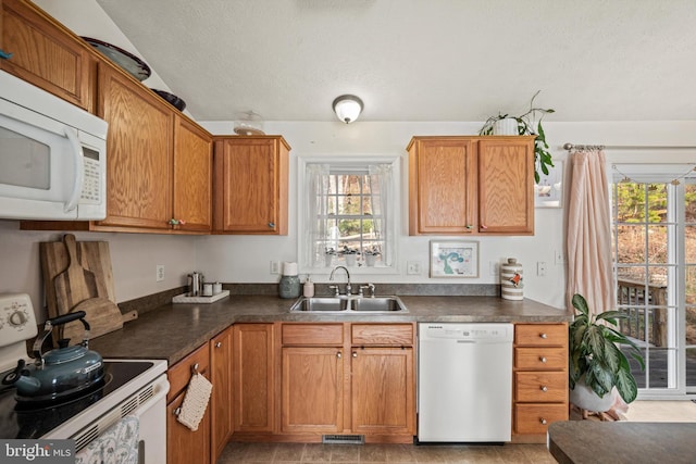 kitchen with a textured ceiling, plenty of natural light, white appliances, and sink