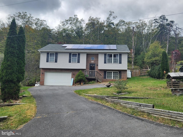 raised ranch with a front yard, solar panels, and a garage