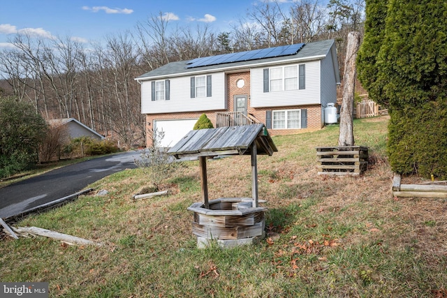 raised ranch with solar panels, a garage, and a front yard