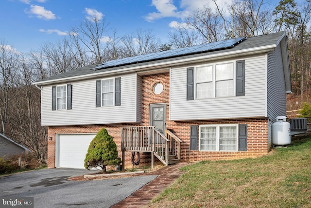 split foyer home with solar panels, cooling unit, a garage, and a front yard