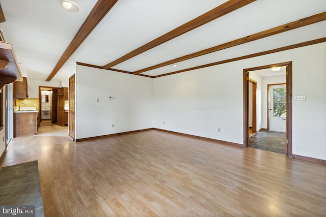 unfurnished living room featuring beamed ceiling, light hardwood / wood-style floors, and sink