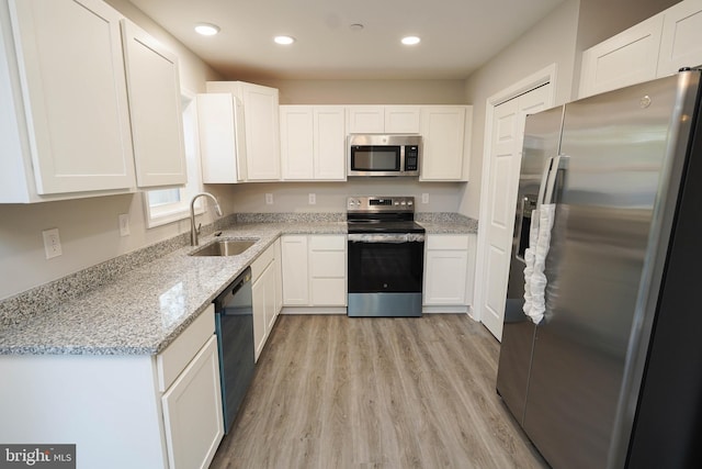 kitchen with light stone countertops, white cabinetry, sink, light hardwood / wood-style flooring, and appliances with stainless steel finishes