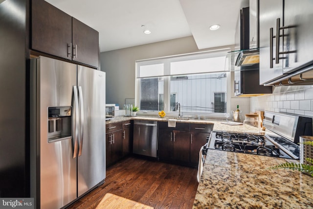 kitchen featuring appliances with stainless steel finishes, backsplash, dark hardwood / wood-style flooring, dark brown cabinets, and light stone countertops