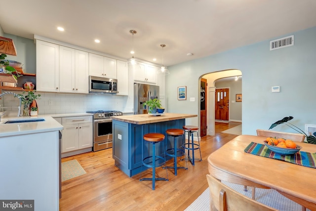 kitchen with appliances with stainless steel finishes, sink, white cabinets, and decorative light fixtures