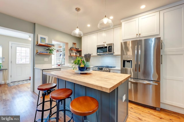 kitchen featuring white cabinetry, wooden counters, a kitchen island, pendant lighting, and stainless steel appliances