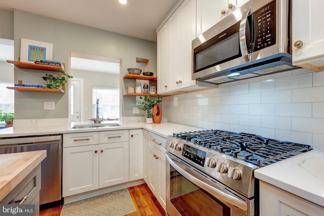 kitchen with sink, appliances with stainless steel finishes, white cabinetry, decorative backsplash, and light wood-type flooring