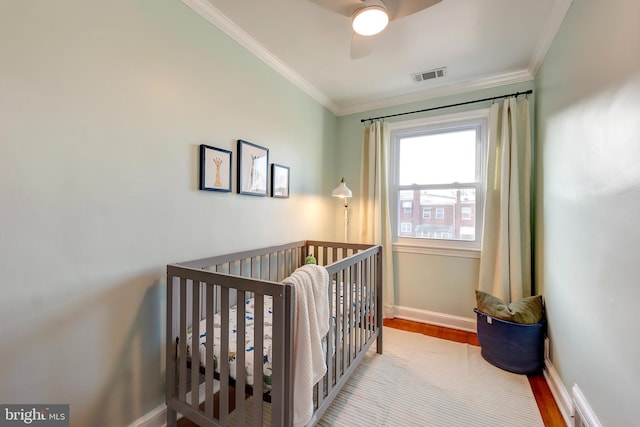 bedroom with a nursery area, ceiling fan, ornamental molding, and light wood-type flooring