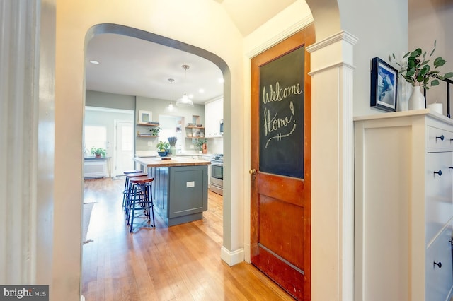 bar featuring pendant lighting, butcher block countertops, stainless steel stove, light hardwood / wood-style flooring, and white cabinetry