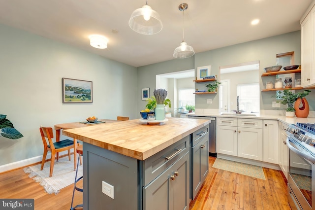 kitchen with sink, appliances with stainless steel finishes, white cabinets, wood counters, and decorative light fixtures