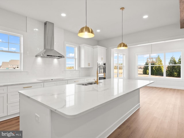 kitchen featuring black electric stovetop, light stone counters, wall chimney exhaust hood, pendant lighting, and white cabinetry