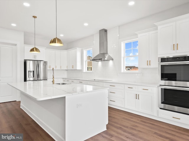 kitchen featuring sink, wall chimney exhaust hood, an island with sink, white cabinets, and appliances with stainless steel finishes