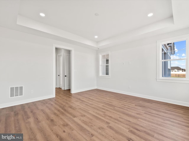 empty room with a raised ceiling and light hardwood / wood-style floors