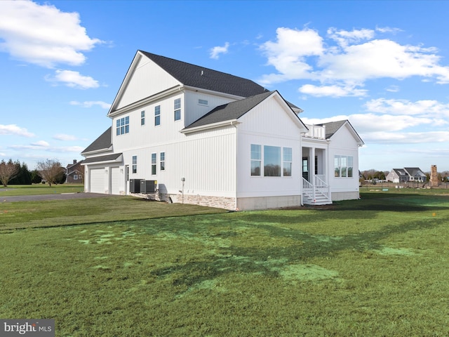 rear view of house with central AC, a garage, and a lawn