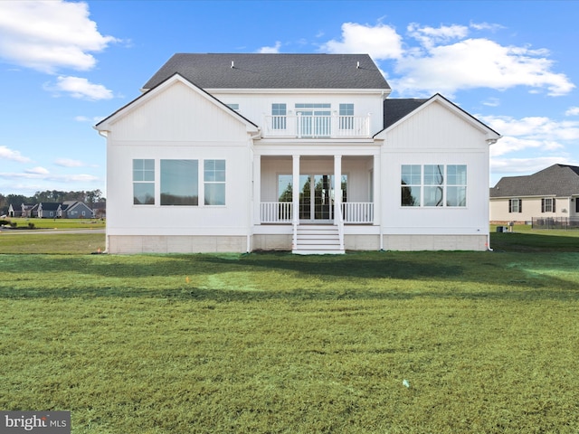 back of house with covered porch, a balcony, and a lawn