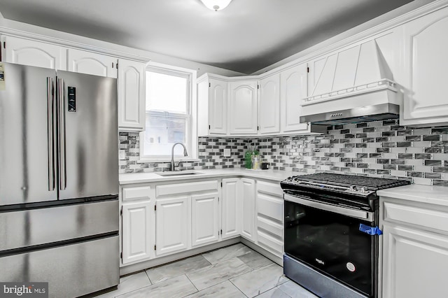 kitchen with sink, black range oven, stainless steel fridge, white cabinets, and custom range hood