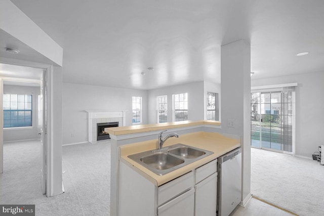 kitchen with dishwasher, a tile fireplace, white cabinets, sink, and light colored carpet