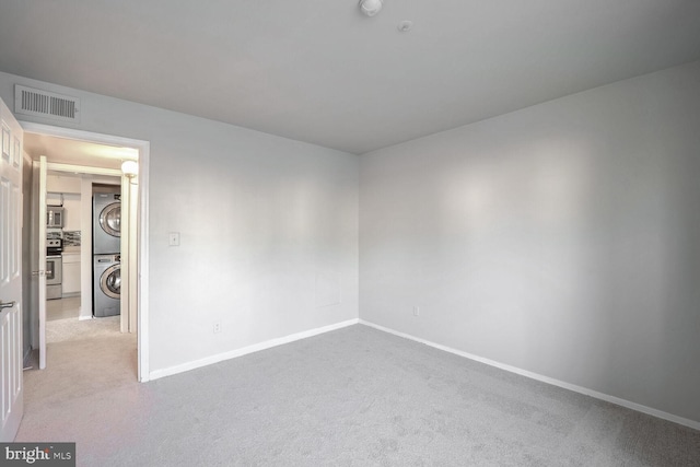 carpeted spare room featuring stacked washing maching and dryer