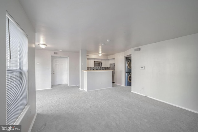 unfurnished living room featuring light carpet and stacked washer and clothes dryer