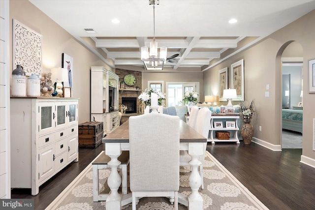 dining room with coffered ceiling, an inviting chandelier, dark hardwood / wood-style floors, a fireplace, and beamed ceiling