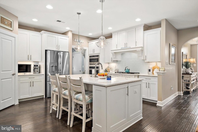 kitchen with pendant lighting, stainless steel appliances, white cabinetry, and a center island with sink